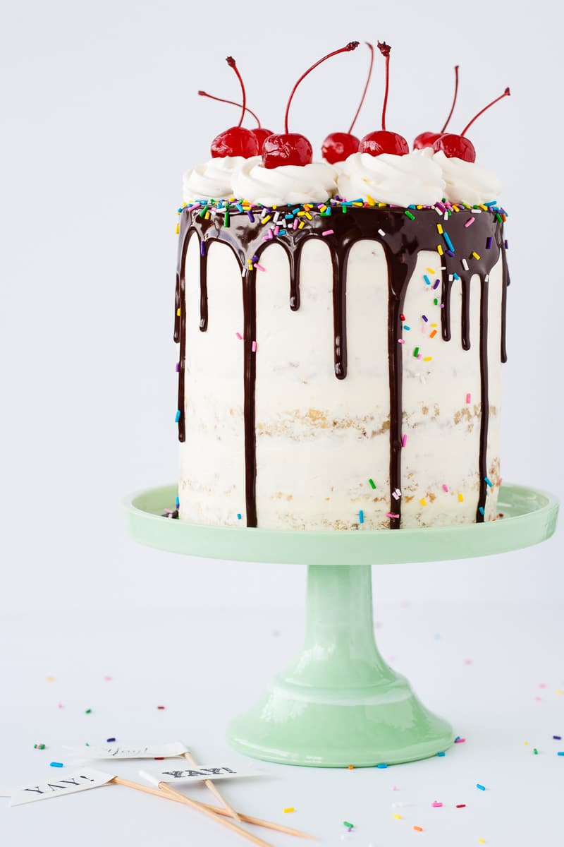 A cake sitting on top of a mint green cake stand with a small bowl of cherries beside it.