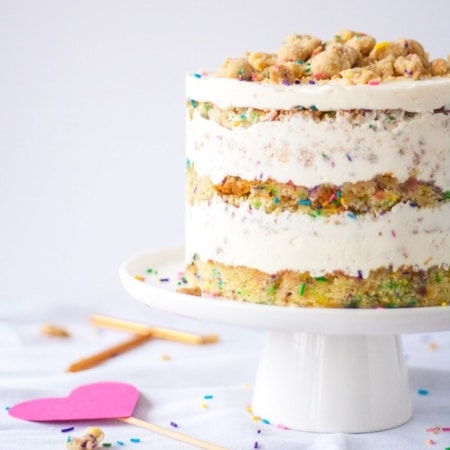 Naked cake on a white cake stand with sprinkles on the table.