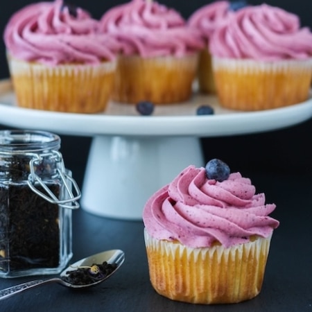 Cupcake in the foreground with cupcakes on a cake stand in the background.