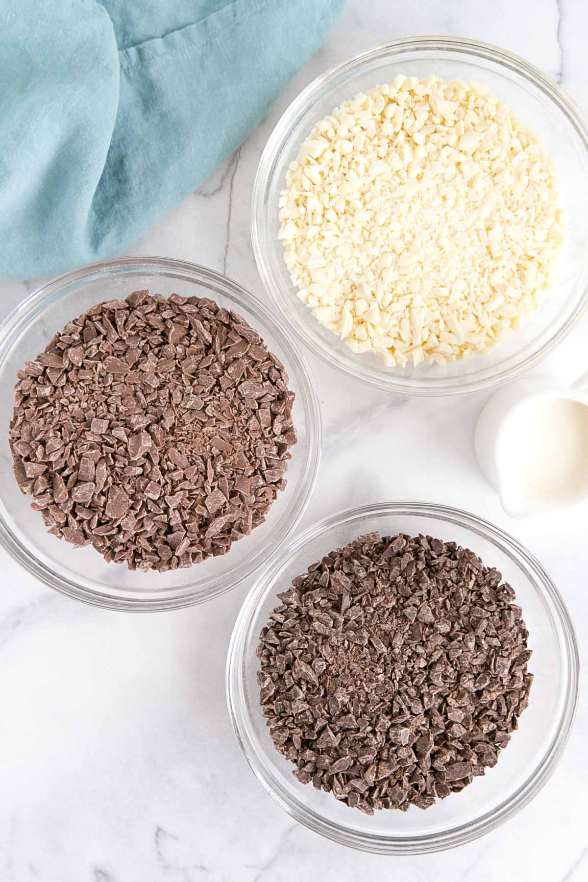 Dark, milk, and white chocolate chopped up in separate bowls.