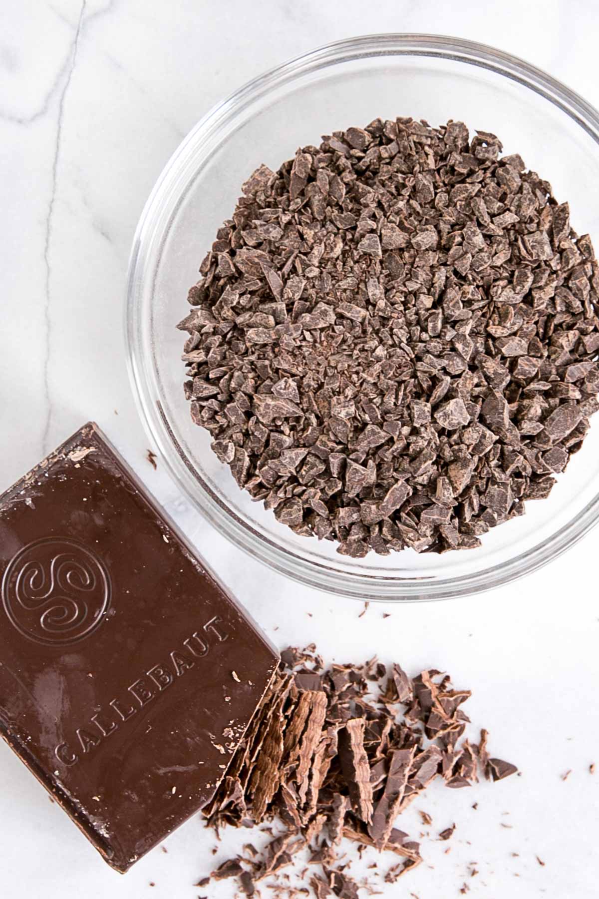 Dark chocolate chopped up in a glass bowl with a dark chocolate bar beside it.