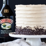 Cake on a white cake stand with a bottle on Baileys behind it.