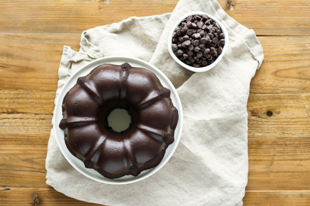 Overhead shot of a bundt cake on a white cake stand with a bowl of chocolate chips beside.