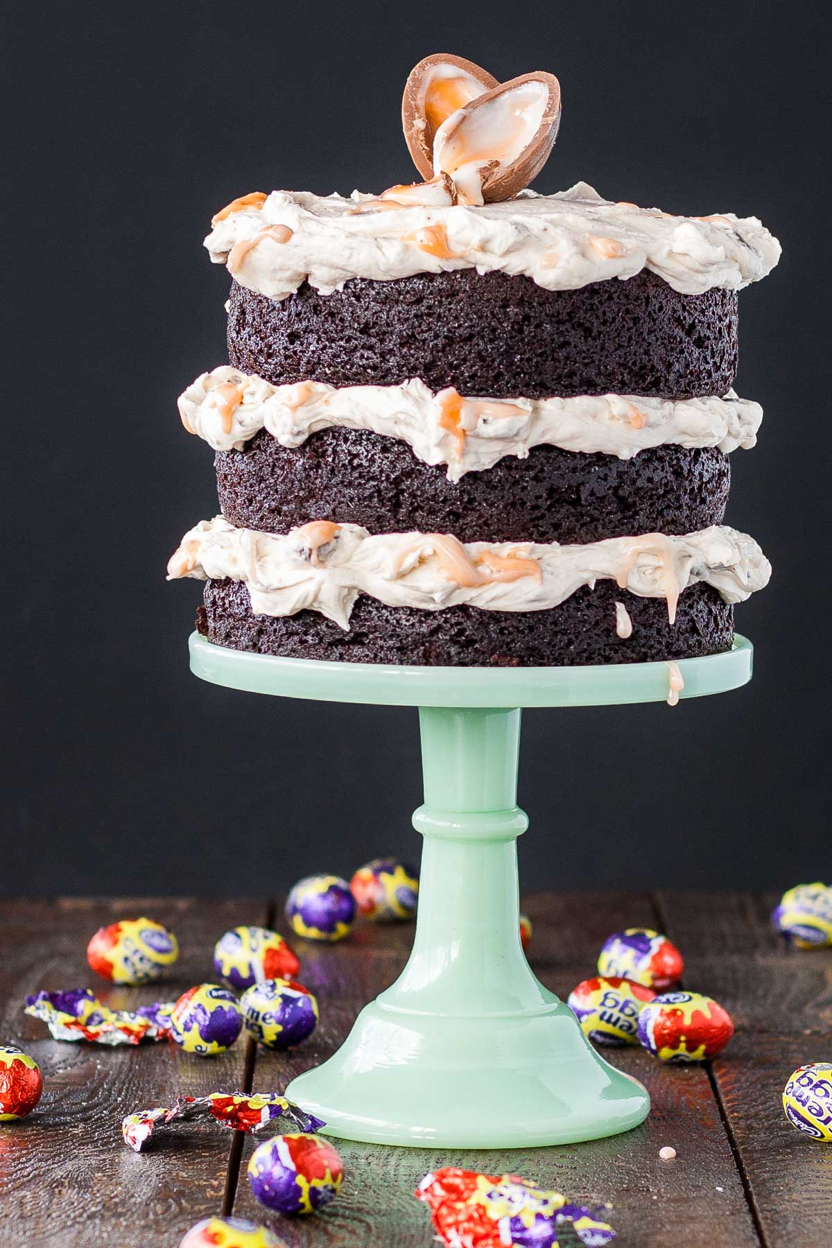 A cake sitting on top of a mint green cake stand. Creme eggs scattered all around.