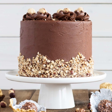 Cake on a white cake stand with opened Ferreros' in the foreground.