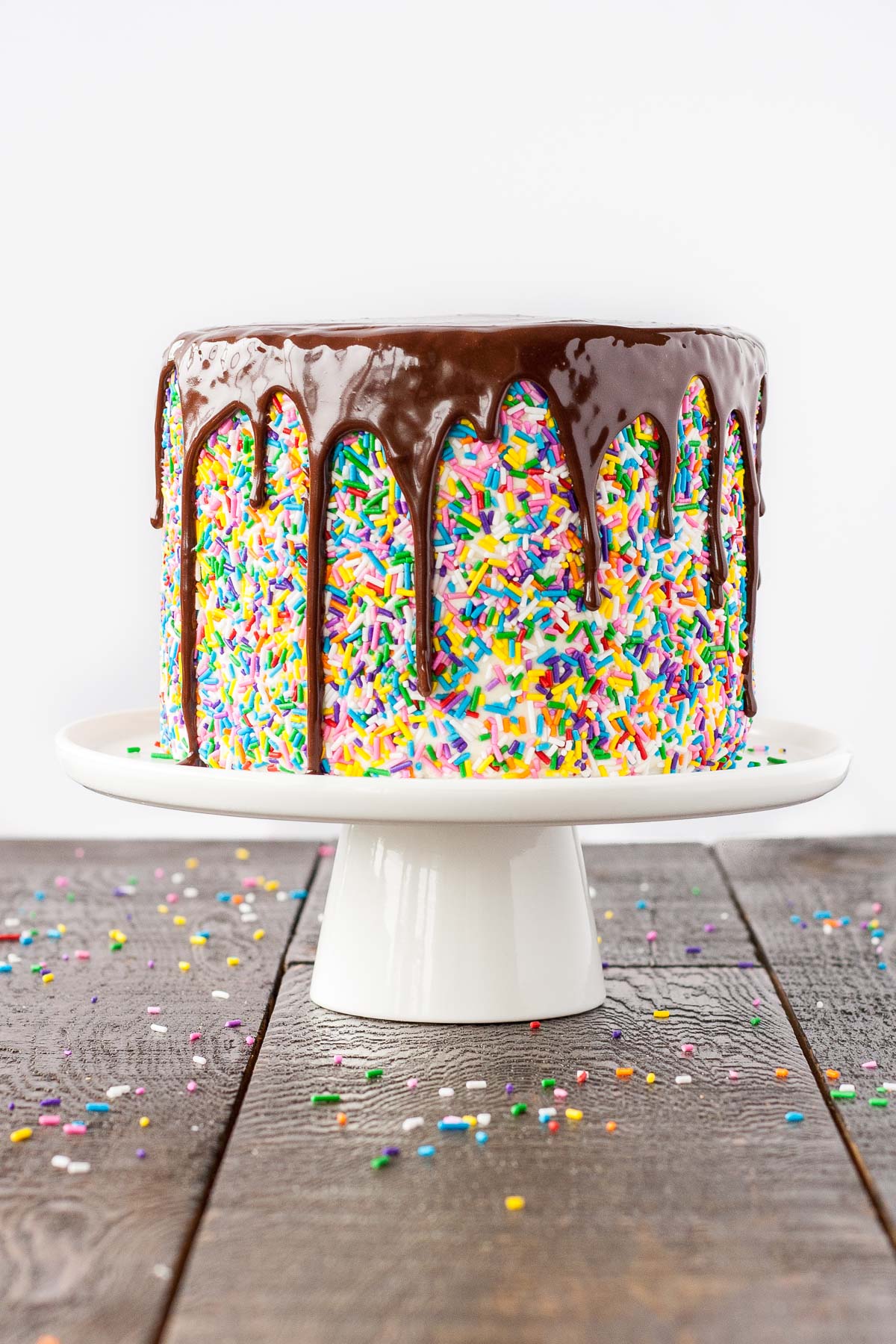 Funfetti cake with a chocolate ganache drip on a white cake stand.