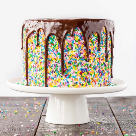 Funfetti cake with a chocolate ganache drip on a white cake stand.