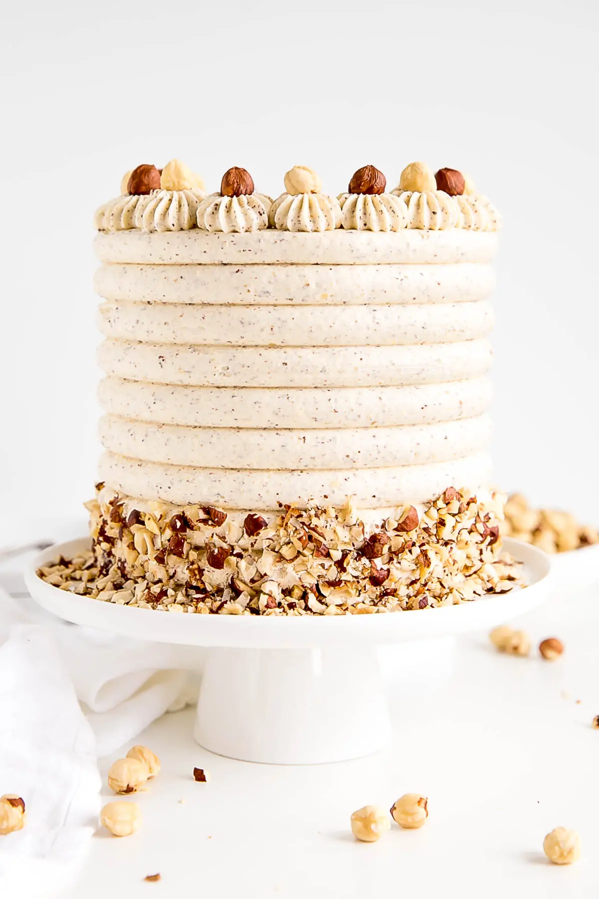 Cake on a white cake stand with a white cloth in the background.