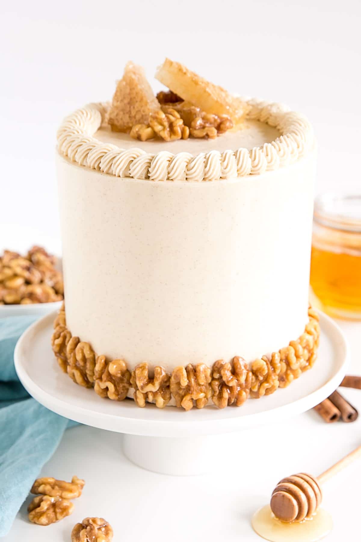 Cake on a cake stand with a blue cloth beside it and a pot of honey behind.