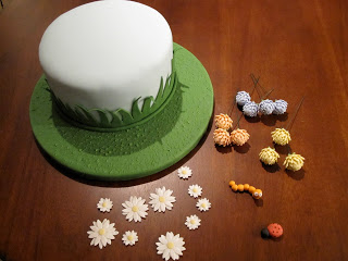 Cake with fondant flowers and bugs ready to be placed on it.