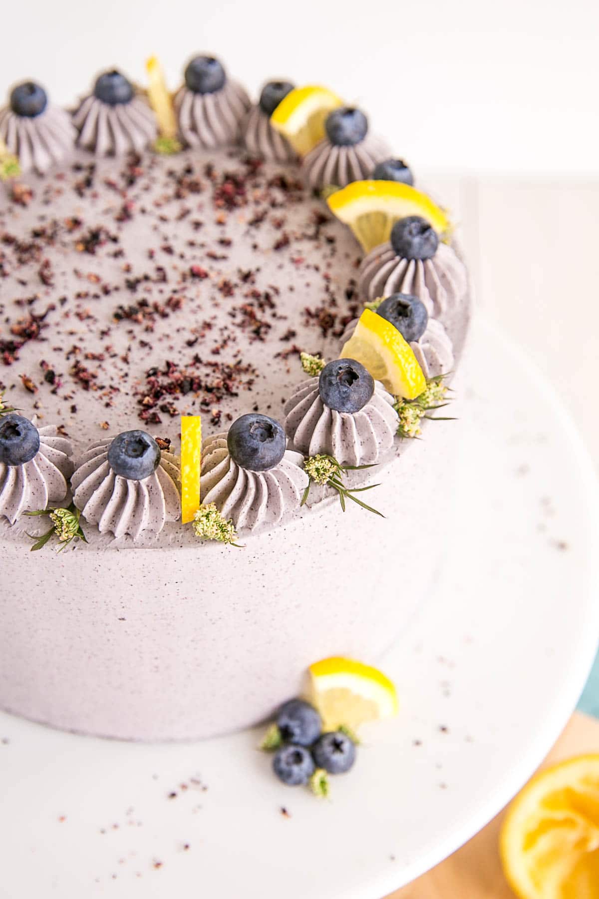 Shot of the top of the cake with blueberries inside buttercream dollops and lemon wedges separating the dollops.