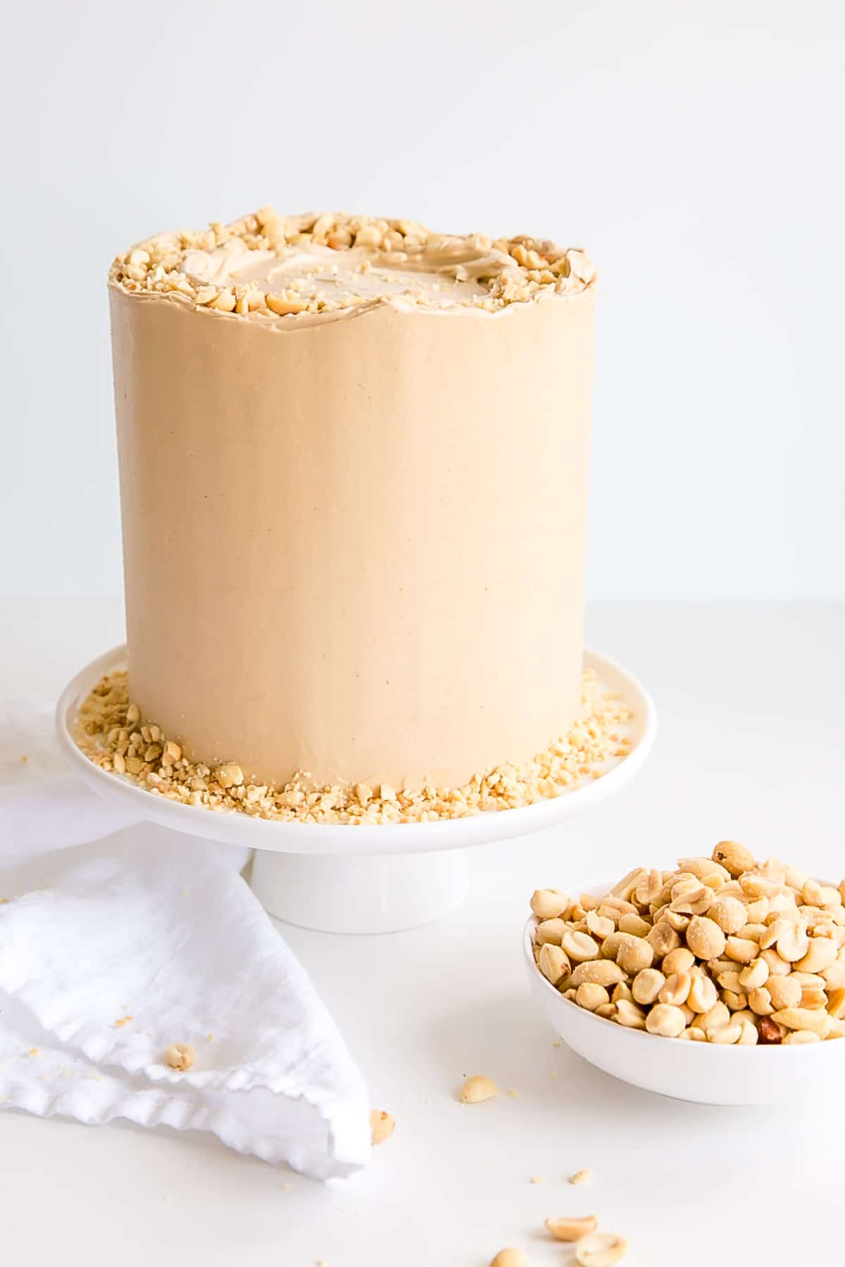 Cake on a white cake stand with a bowl of peanuts next to it.