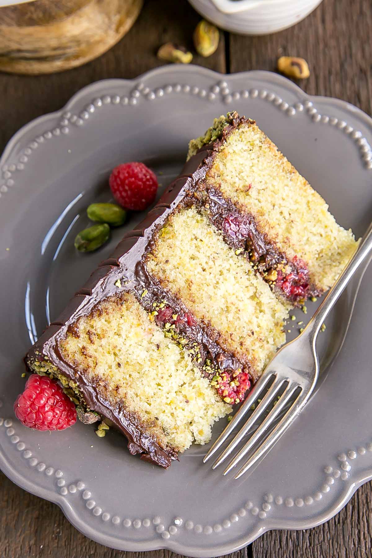 Cut slice of Pistachio Cake with Dark Chocolate Ganache and fresh Raspberries.