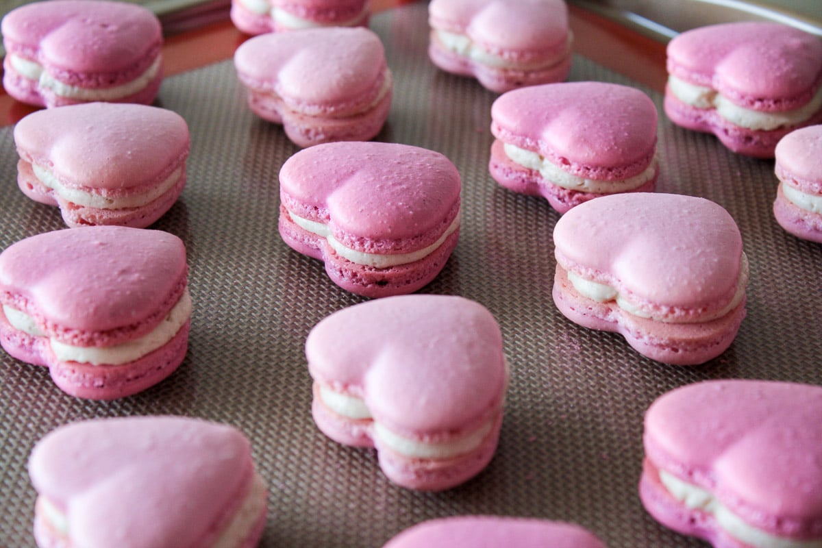 Sandwiched heart macarons on a baking sheet.